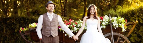 Svatební pár ve stylovém oblečení u dřevěného povozu