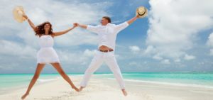 Mladý svatební pár na pláži s klobouky ve výskoku