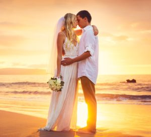Novomanželé v objetí na břehu moře při západu slunce