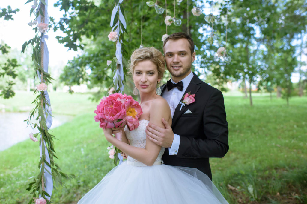 Svatební pár v přírodě, nevěsta s kyticí pivoněk