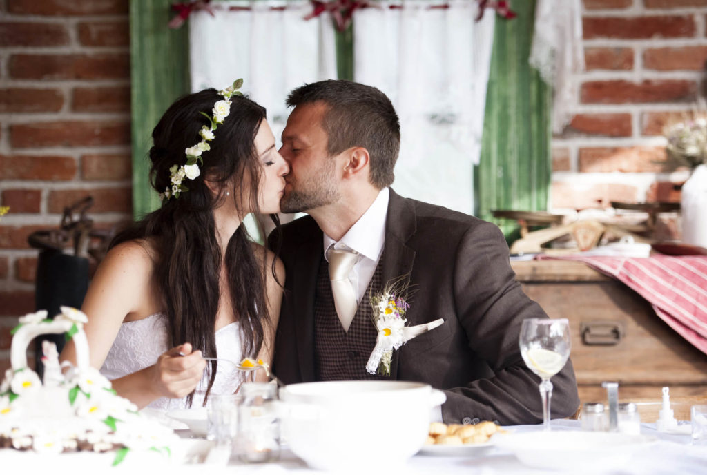 Nevěsta s ženichem při polibku na venkovské svatbě u cihlové zdi
