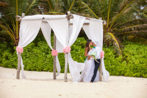 Svatba v zahraničí, novomanželé v objetí na pláži pod palmami