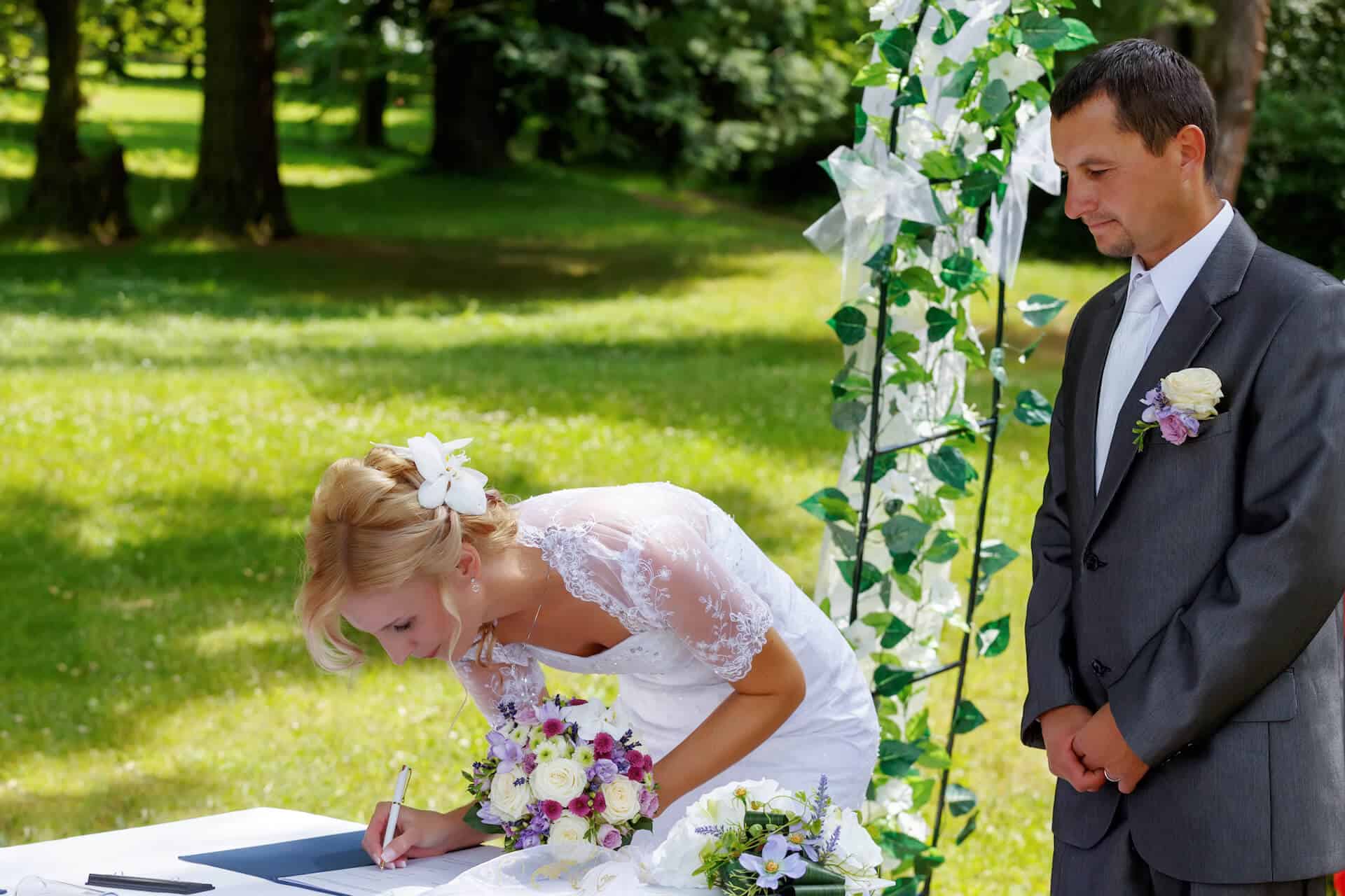 Nevěsta podepisuje vstup do manželství při svatebních obřadu na zahradě