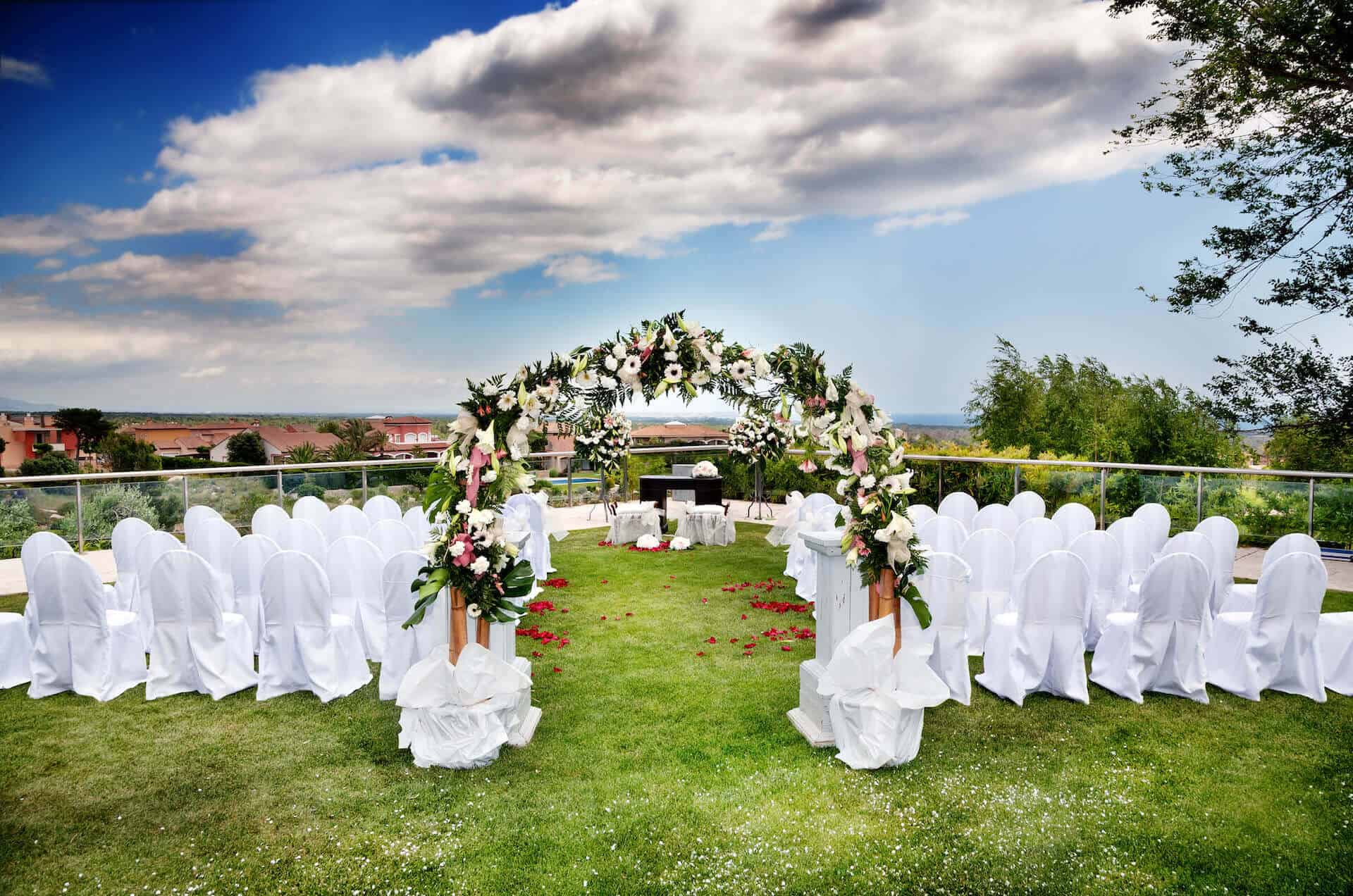 Venkovní svatební obřad, květinová svatební slavobrána a židle se svatebními potahy
